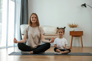 Sticker - Calm, in lotus pose. Young woman with little girl are doing yoga at home