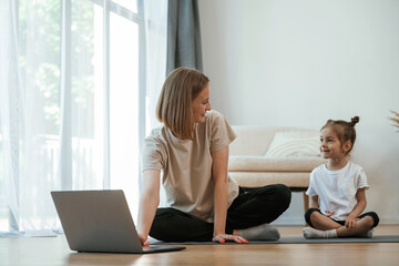 Wall Mural - Using laptop. Young woman with little girl are doing yoga at home