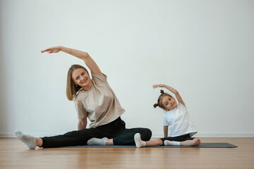 Sticker - To the side, stretching. Young woman with little girl are doing yoga at home