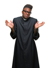 Wall Mural - Young african american priest man over isolated background clueless and confused expression with arms and hands raised. Doubt concept.