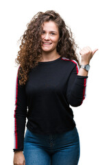 Poster - Beautiful young brunette curly hair girl wearing casual look over isolated background smiling with happy face looking and pointing to the side with thumb up.