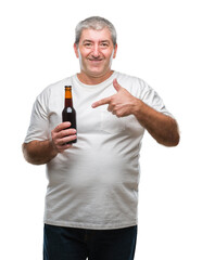 Canvas Print - Handsome senior man drinking beer bottle over isolated background very happy pointing with hand and finger