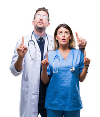 Wall Mural - Young couple of doctor and surgeon over isolated background amazed and surprised looking up and pointing with fingers and raised arms.