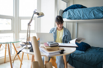 Student asian woman sitting on bed in dorm room college student Work or homework on laptop in university dormitory