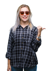 Poster - Young blonde woman wearing sunglasses over isolated background smiling with happy face looking and pointing to the side with thumb up.