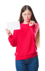 Sticker - Young Chinese woman over isolated background holding blank card pointing with finger to the camera and to you, hand sign, positive and confident gesture from the front