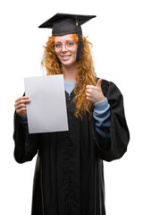 Wall Mural - Young redhead woman wearing graduate uniform holding degree happy with big smile doing ok sign, thumb up with fingers, excellent sign