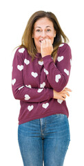 Canvas Print - Beautiful middle age woman wearing hearts sweater over isolated background looking stressed and nervous with hands on mouth biting nails. Anxiety problem.