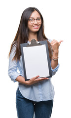 Sticker - Young asian business woman holding clipboard over isolated background pointing and showing with thumb up to the side with happy face smiling