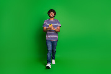 Sticker - Portrait photo of young indian curly funny man student in striped t shirt chatting with smartphone isolated on green color background