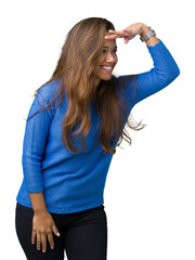 Wall Mural - Young beautiful brunette woman wearing blue sweater over isolated background very happy and smiling looking far away with hand over head. Searching concept.