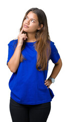 Canvas Print - Young beautiful brunette woman wearing blue t-shirt over isolated background with hand on chin thinking about question, pensive expression. Smiling with thoughtful face. Doubt concept.