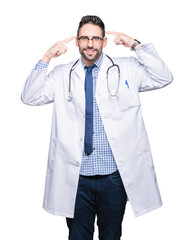 Wall Mural - Handsome young doctor man over isolated background Smiling pointing to head with both hands finger, great idea or thought, good memory