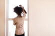 © Dasha Petrenko - A curly-haired mixed-race girl in casual clothes wipes the window with a rag. A young African woman cleans a house or apartment.