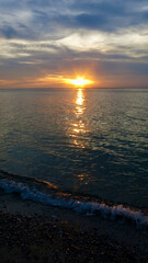 Wall Mural - Sunset over the sea. View from the beach of the sun setting among the clouds behind the horizon. The sun reflects on the surface of the sea during sunset.