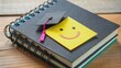 © Adisorn - Colorful adhesive note with a smiling face sticker on a printed and bound bachelor thesis with a black cover, symbolizing accomplishment and new beginnings.
