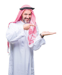 Wall Mural - Senior arab man wearing keffiyeh over isolated background amazed and smiling to the camera while presenting with hand and pointing with finger.