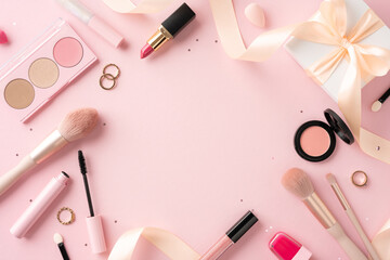 A beautiful collection of makeup and cosmetics tools arranged artfully on a pastel pink background with a gift box