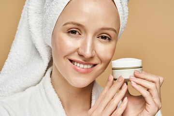 Wall Mural - A woman with a towel on her head holds a jar of cream, embodying natural beauty and indulging in a self-care routine.