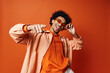 © LIGHTFIELD STUDIOS - A stylish young African American man with curly hair wearing an orange shirt and sunglasses, posing energetically against an orange background.