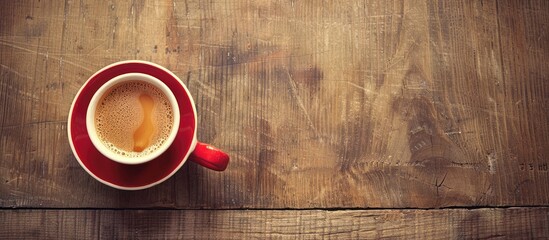 Wall Mural - Vintage toned top down shot of a hot coffee filled red cup on a wooden table featuring copy space image