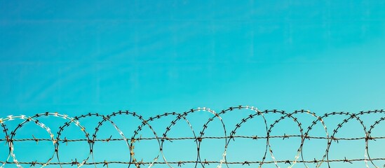 Poster - Barbed wire against a clear blue sky is commonly seen bordering prisons country boundaries or private properties creating a visual with ample copy space for themes like restricted areas illegal immig