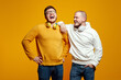 © Davidovici - Two excited friends in casual wear standing and laughing together. Best friends enjoying isolated over yellow background. Two men with headphones having fun in studio. Friendship concept