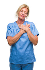 Wall Mural - Middle age blonde woman wearing doctor nurse uniform over isolated background smiling with hands on chest with closed eyes and grateful gesture on face. Health concept.