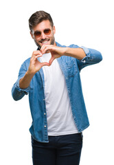 Sticker - Young handsome man wearing sunglasses over isolated background smiling in love showing heart symbol and shape with hands. Romantic concept.