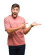 © Krakenimages.com - Young handsome man over isolated background amazed and smiling to the camera while presenting with hand and pointing with finger.