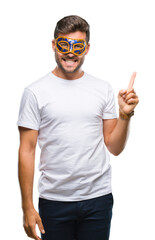 Canvas Print - Young handsome man wearing carnival mask over isolated background with a big smile on face, pointing with hand and finger to the side looking at the camera.