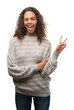 © Krakenimages.com - Beautiful young hispanic woman wearing stripes sweater smiling with happy face winking at the camera doing victory sign. Number two.