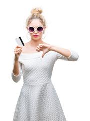 Sticker - Young beautiful blonde woman holding credit card over isolated background with angry face, negative sign showing dislike with thumbs down, rejection concept