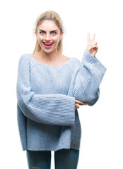 Wall Mural - Young beautiful blonde and blue eyes woman wearing winter sweater over isolated background smiling with happy face winking at the camera doing victory sign. Number two.