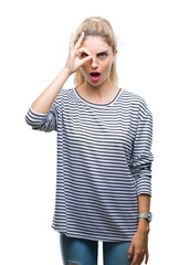 Canvas Print - Young beautiful blonde woman wearing stripes sweater over isolated background doing ok gesture shocked with surprised face, eye looking through fingers. Unbelieving expression.