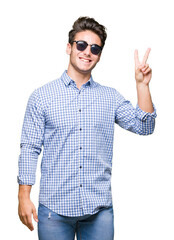 Wall Mural - Young handsome man wearing sunglasses over isolated background smiling with happy face winking at the camera doing victory sign. Number two.