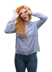 Canvas Print - Young redhead bussines woman doing ok gesture shocked with surprised face, eye looking through fingers. Unbelieving expression.