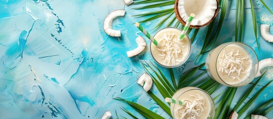 Aufkleber - White tropical cocktail made with coconut milk served in glasses with straws on a blue background adorned with coconut and palm leaves offering a top view and ample copy space image