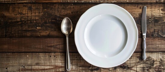 Leinwandbilder - Top down view of a white plate with a spoon and fork placed on a wooden table to convey a food concept with a space for additional images