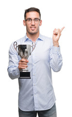 Sticker - Handsome young man holding trophy very happy pointing with hand and finger to the side