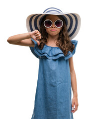 Poster - Brunette hispanic girl wearing sunglasses and summer hat with angry face, negative sign showing dislike with thumbs down, rejection concept