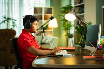 Wall Mural - ndian Asian teenage student learning online with computer, headphones, and smartphone