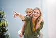 © AK Coop/peopleimages.com - Happy mother, pointing and piggyback with daughter for bonding, holiday or weekend in backyard at home. Mom, child or little girl with smile for back ride, playing or support for outdoor day together