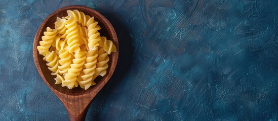 Wall Mural - Top down view of dry pasta in a wooden spoon on a blue textured background with a designated area for additional text or images