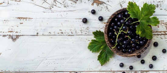 Poster - Top down view of a wooden bowl containing black currants accompanied by a green leaf set against a white wooden backdrop Ideal for copy space imagery