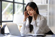 © Wasan - A woman in the office is stressed and has a headache from overwork. Tired business woman sleepy and bored from sitting at a desk for a long time and has office syndrome.