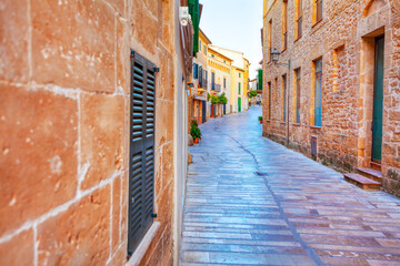 Sticker - Narrow street with a brick wall on the side. The street is empty and the buildings are old. Old town of Mallorca island