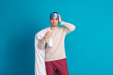 Poster - Photo portrait of handsome young guy hold duvet depressed dressed sleepwear sleepover good morning isolated on blue color background