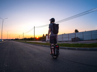 Wall Mural - A man rides an electric monocycle on the road at sunset. Wearing a helmet and knee pads. Urban mobile transport.