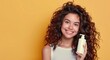 © ArtCookStudio - Smiling Woman With Curly Hair Holding White Bottle Against Yellow Background